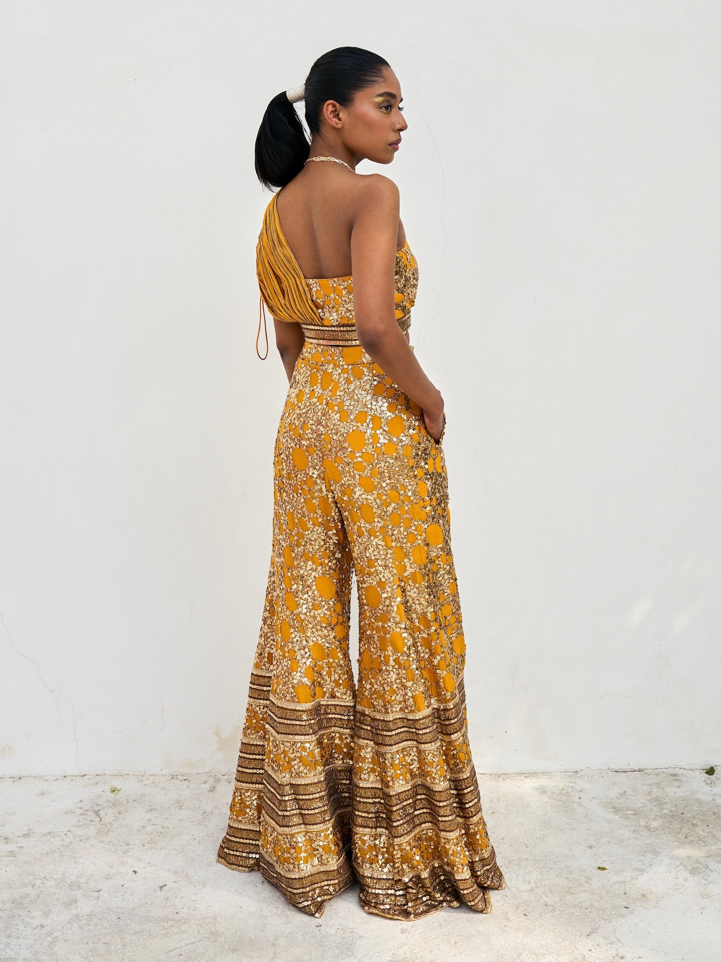 The sequined Tanvi Palazzo Set consists of a one-shoulder adjustable top and flared palazzo pants.