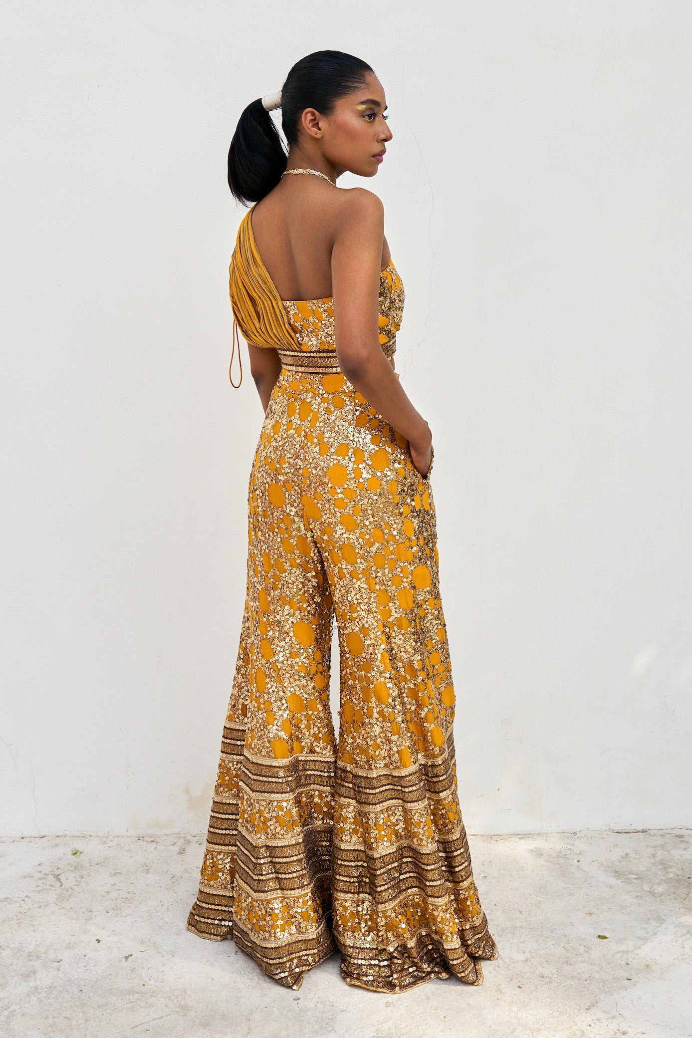 The sequined Tanvi Palazzo Set consists of a one-shoulder adjustable top and flared palazzo pants.