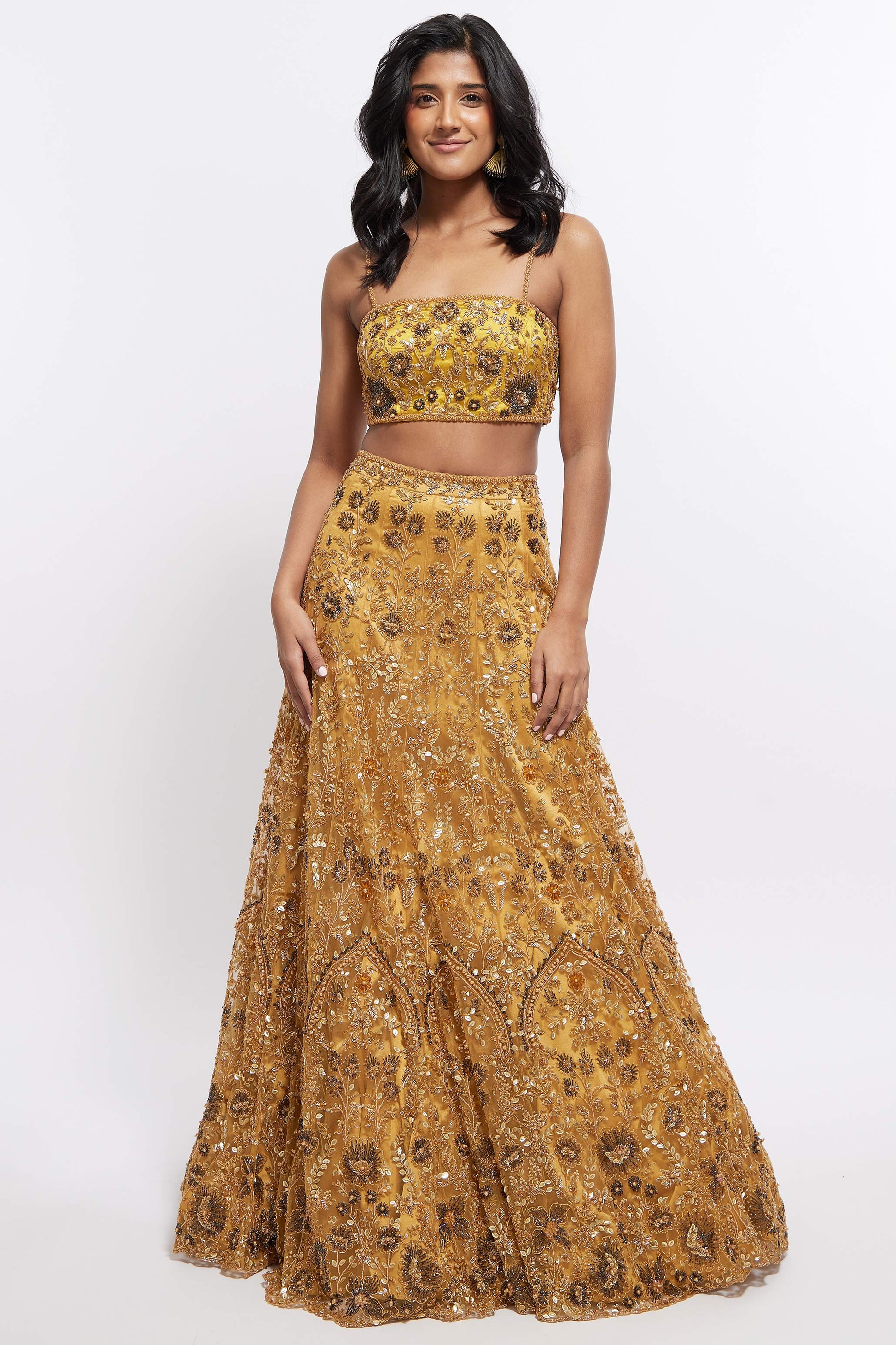 The Hasina Lehenga showcases intricate three-dimensional embroidery, comprising crystal, sequin, and beadwork in an ornate floral pattern adorning both the blouse and skirt. It is elegantly complemented by a matching skinny dupatta with beaded tassels.