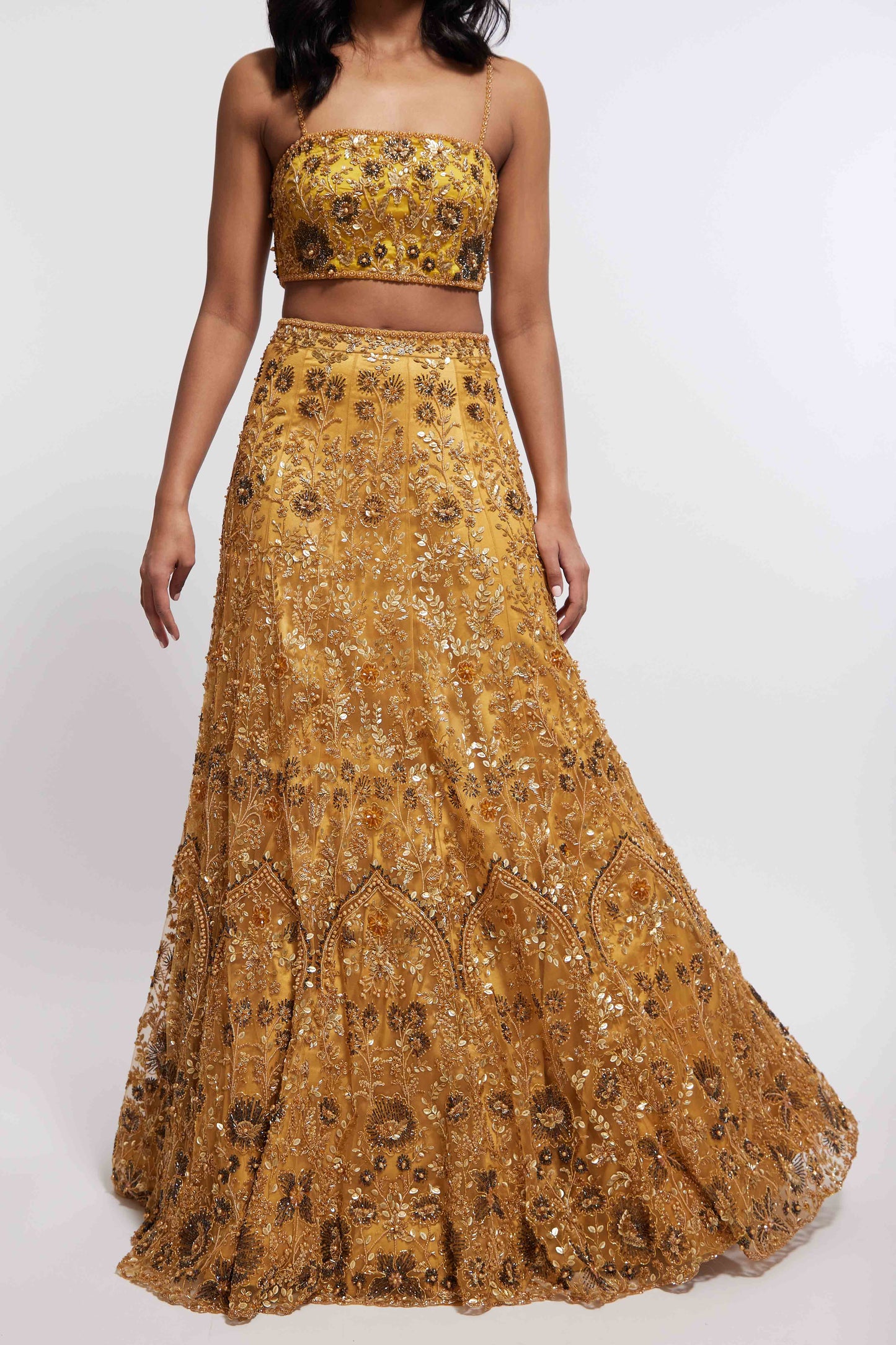 The Hasina Lehenga showcases intricate three-dimensional embroidery, comprising crystal, sequin, and beadwork in an ornate floral pattern adorning both the blouse and skirt. It is elegantly complemented by a matching skinny dupatta with beaded tassels.