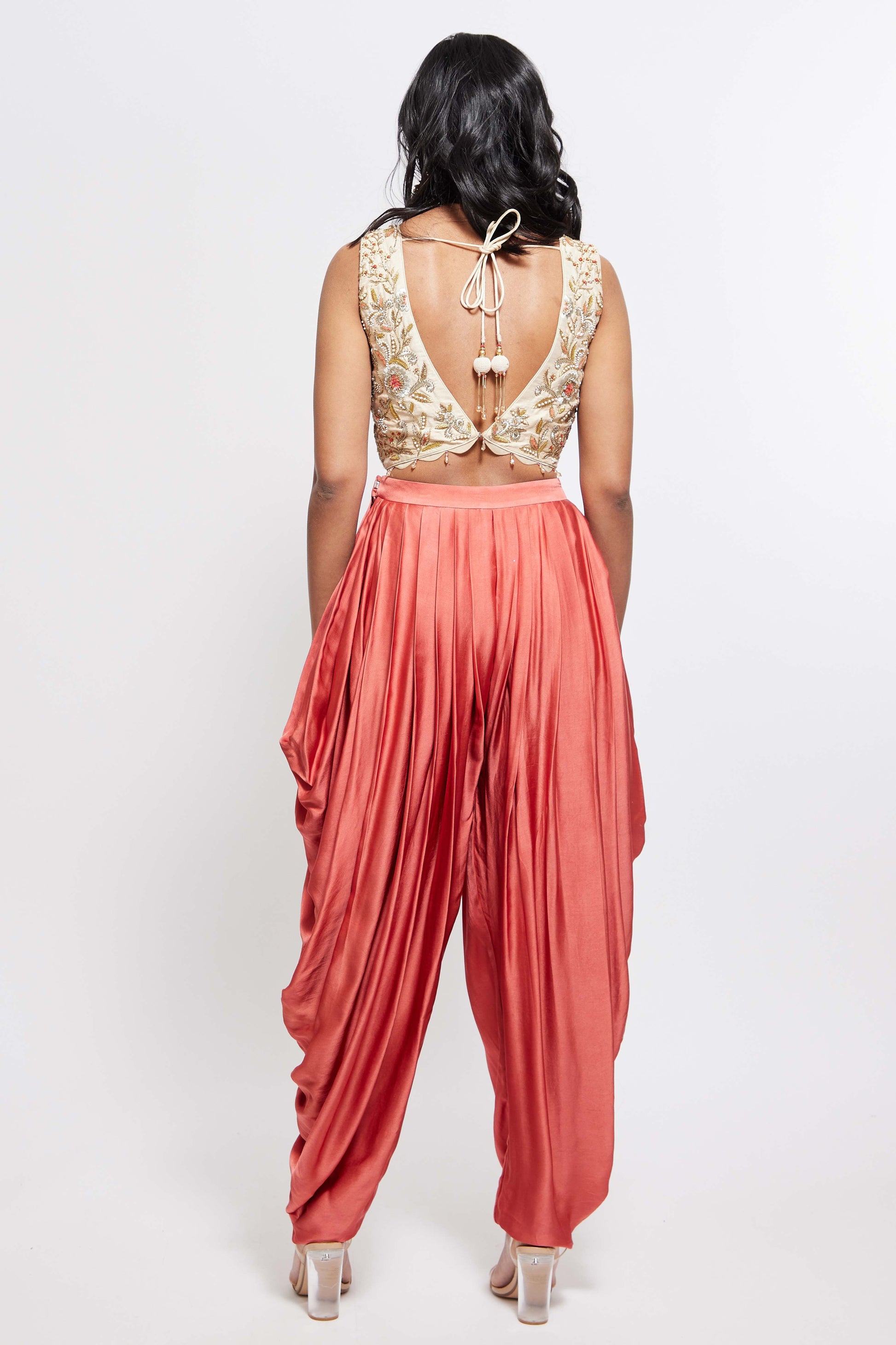 The Sneh Dhoti takes the elegance of a saree's drape and combines it with the comfort of a dhoti pant. Made from bamboo satin, the dhoti pant is paired with a hand-embroidered blouse featuring scalloped edges, floral motifs, and crystal beadwork. This outfit includes an organza dupatta adorned with scattered floral motifs and delicate beadwork. Its ruffle trim offers versatility, allowing it to be styled as a shawl.
