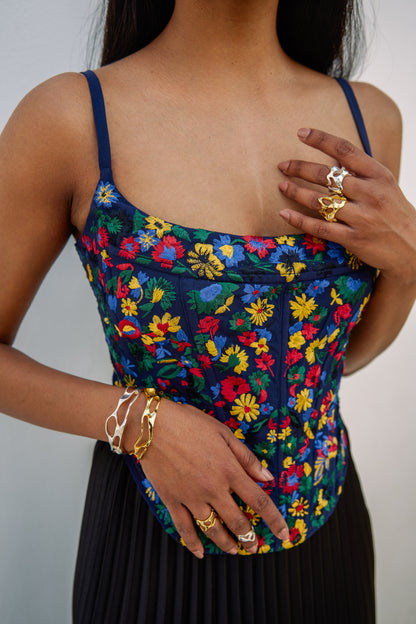 The Zinnia Top is a corset style with embroidered, multicolored flowers and adjustable straps. 