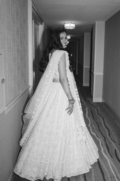 The Rucha Lehenga is a white hand-embroidered lehenga adorned with Swarovski crystals. It features a v-neck blouse with two tie details in the back. It comes with a completely detachable can-can. 