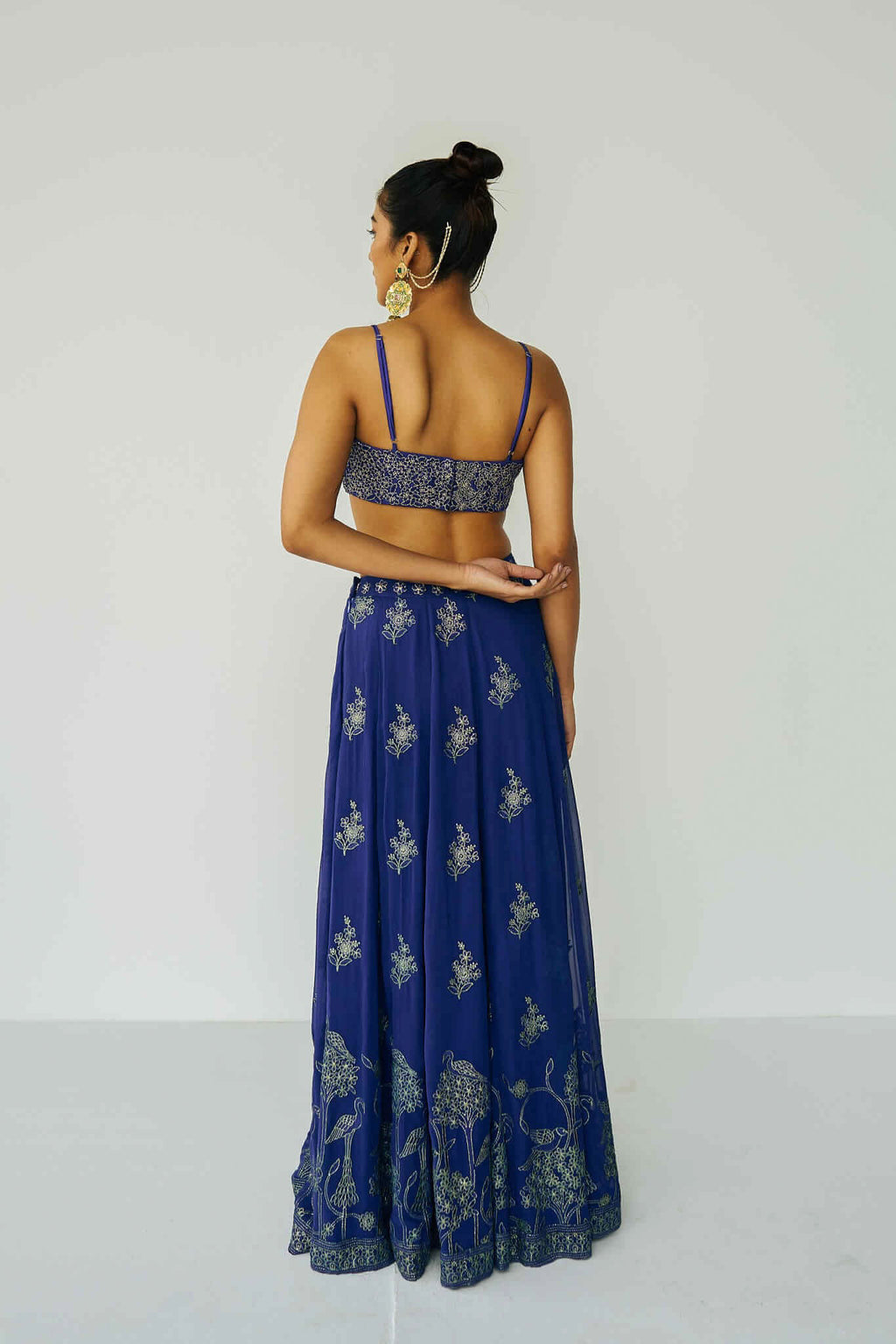 A woman wearing a bright blue embroidered top and skirt with an embroidered dupatta.