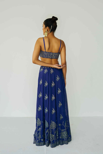 A woman wearing a bright blue embroidered top and skirt with an embroidered dupatta.