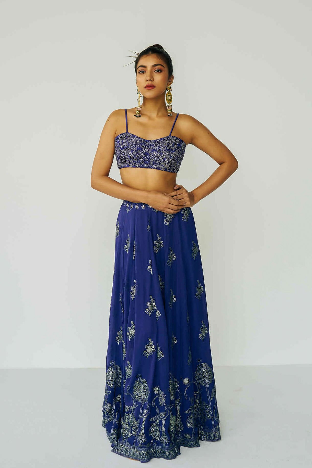 A woman wearing a bright blue embroidered top and skirt with an embroidered dupatta.