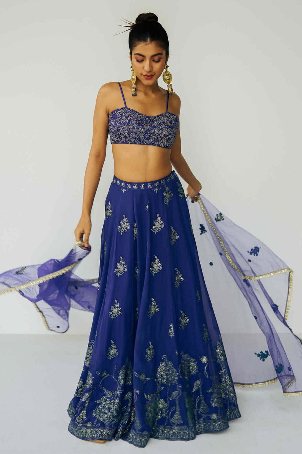 A woman wearing a bright blue embroidered top and skirt with an embroidered dupatta.