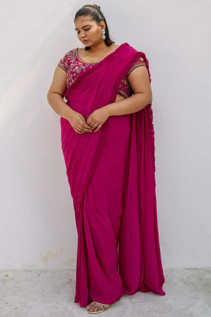 This outfit features a high-waisted skirt with attached wrap-around draping - all pre-stitched so you can put the outfit together in 30 seconds or less. The piece is paired with a pink hand-embroidered, cap-sleeve blouse with a low