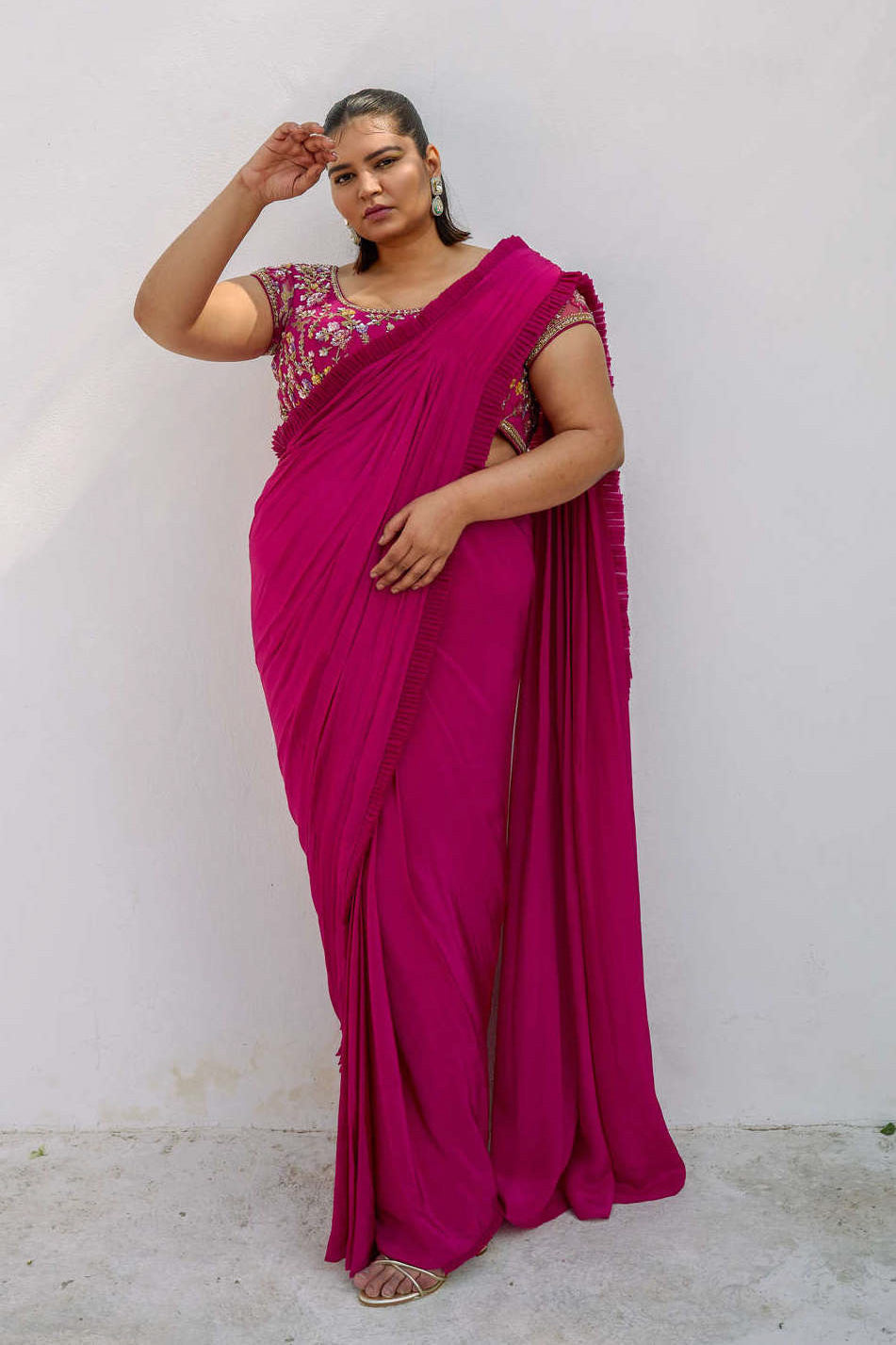 This outfit features a high-waisted skirt with attached wrap-around draping - all pre-stitched so you can put the outfit together in 30 seconds or less. The piece is paired with a pink hand-embroidered, cap-sleeve blouse with a low