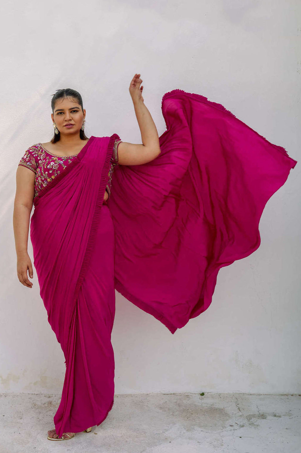 This outfit features a high-waisted skirt with attached wrap-around draping - all pre-stitched so you can put the outfit together in 30 seconds or less. The piece is paired with a pink hand-embroidered, cap-sleeve blouse with a low