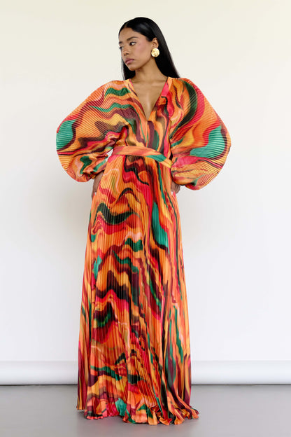 The Sia Dress features a bold abstract print on pleated fabric. Designed with a flattering V-neck, fitted waist, and flowing silhouette, it includes long sleeves, a tie closure at the back, and pockets. Whether you're attending a wedding or heading on a colorful getaway, this dress is an easy statement piece.