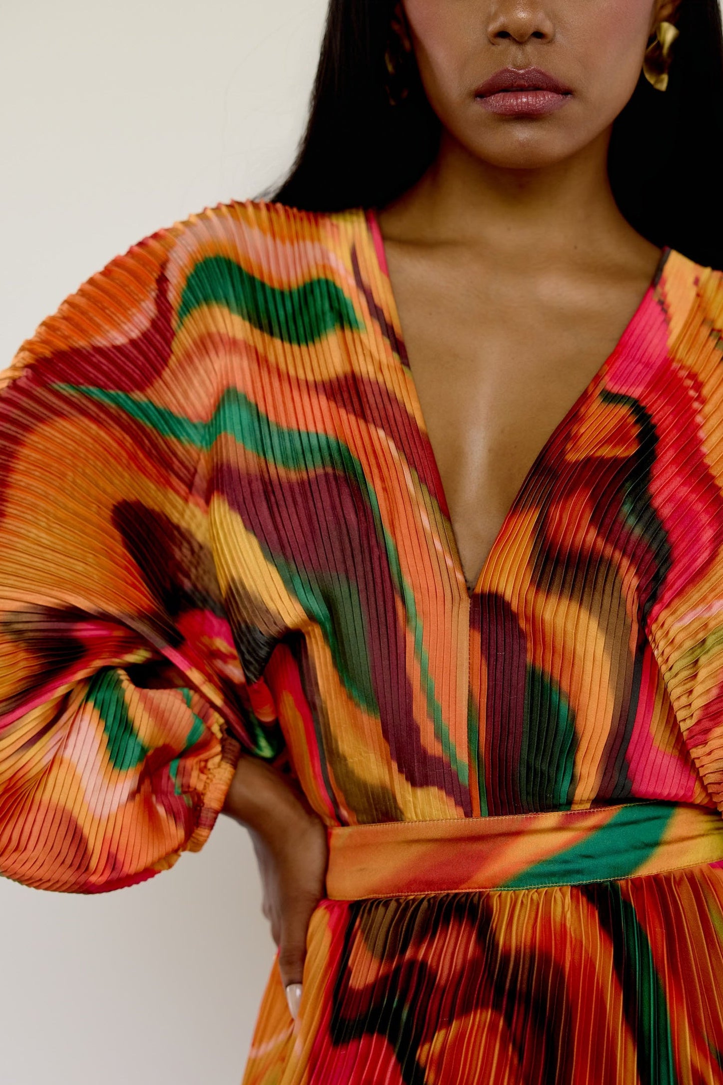 The Sia Dress features a bold abstract print on pleated fabric. Designed with a flattering V-neck, fitted waist, and flowing silhouette, it includes long sleeves, a tie closure at the back, and pockets. Whether you're attending a wedding or heading on a colorful getaway, this dress is an easy statement piece.