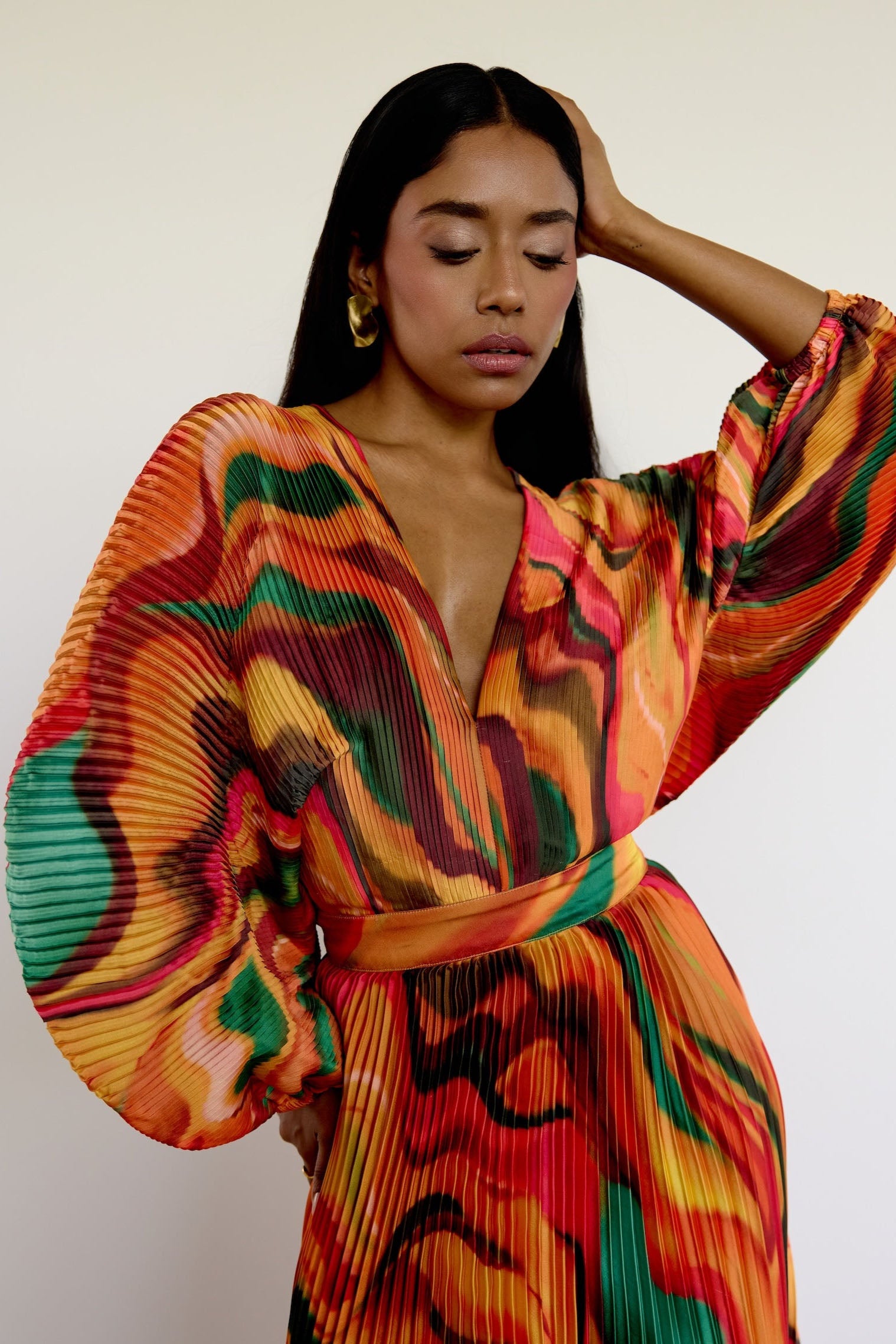 The Sia Dress features a bold abstract print on pleated fabric. Designed with a flattering V-neck, fitted waist, and flowing silhouette, it includes long sleeves, a tie closure at the back, and pockets. Whether you're attending a wedding or heading on a colorful getaway, this dress is an easy statement piece.