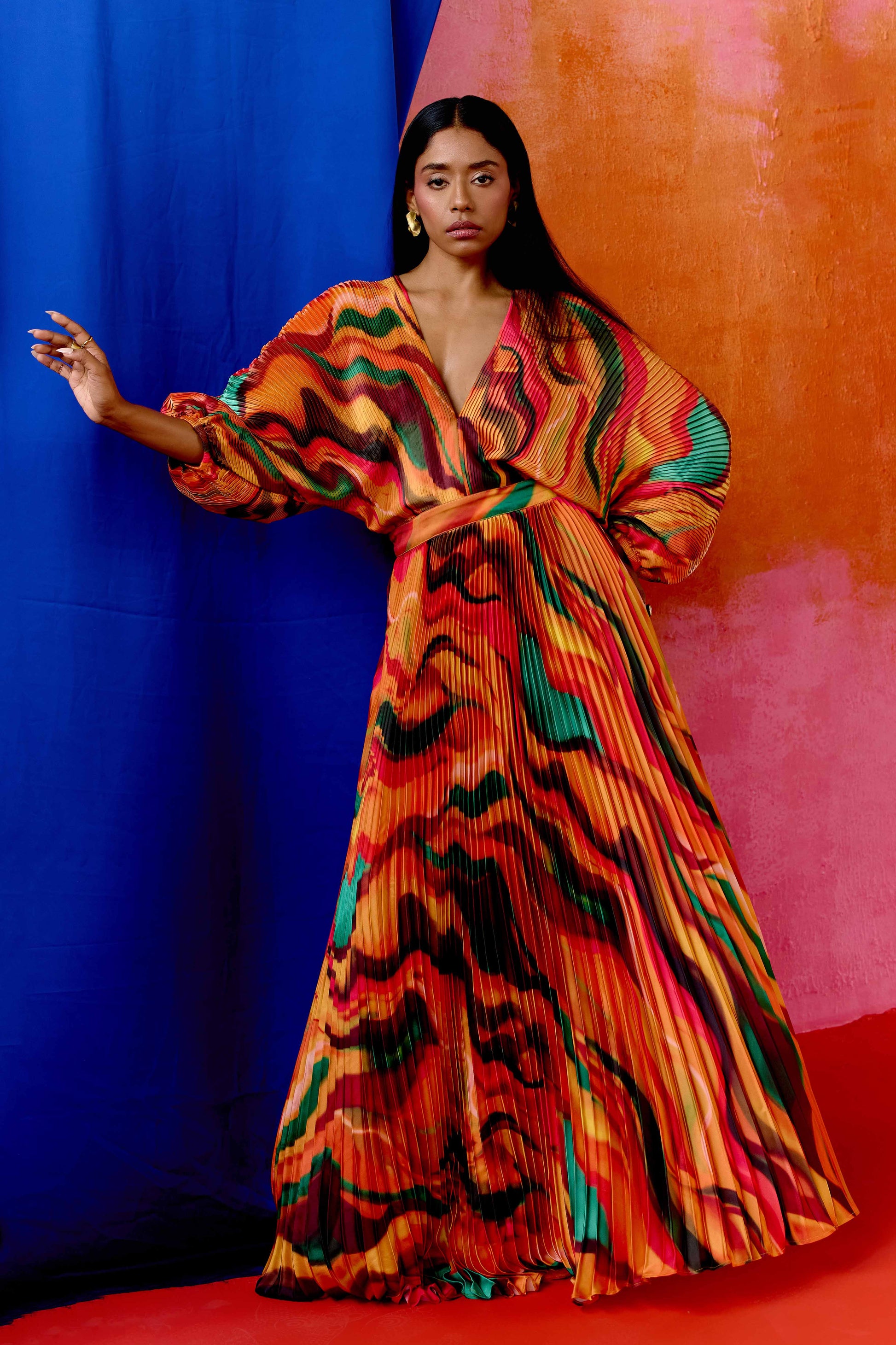 The Sia Dress features a bold abstract print on pleated fabric. Designed with a flattering V-neck, fitted waist, and flowing silhouette, it includes long sleeves, a tie closure at the back, and pockets. Whether you're attending a wedding or heading on a colorful getaway, this dress is an easy statement piece.