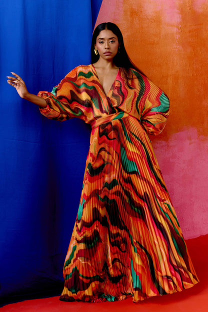 The Sia Dress features a bold abstract print on pleated fabric. Designed with a flattering V-neck, fitted waist, and flowing silhouette, it includes long sleeves, a tie closure at the back, and pockets. Whether you're attending a wedding or heading on a colorful getaway, this dress is an easy statement piece.