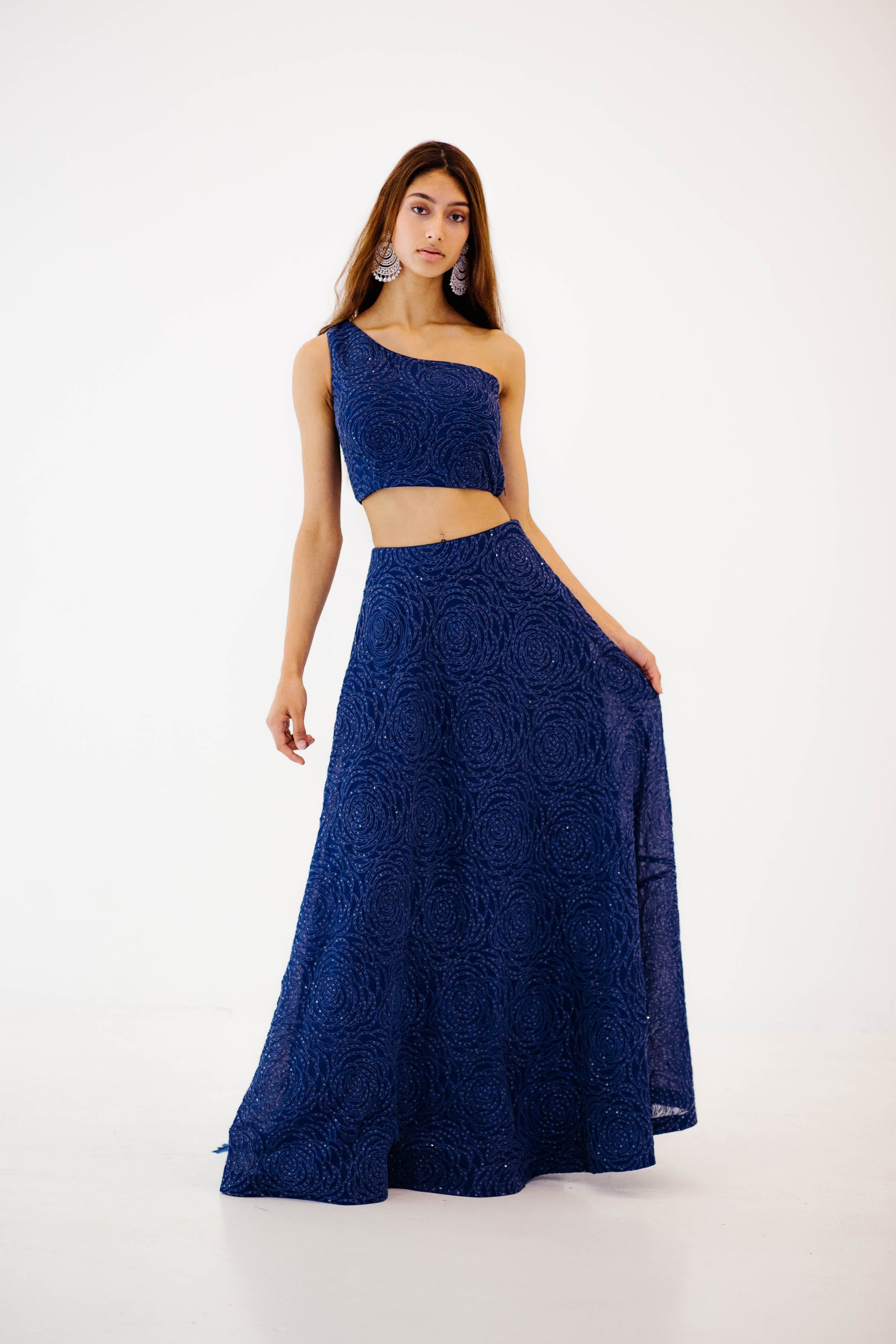 The Raz Lehenga has a dark blue georgette skirt with thread and sequin work in the shape of roses, featuring a one shoulder blouse, and is paired with a matching dupatta.