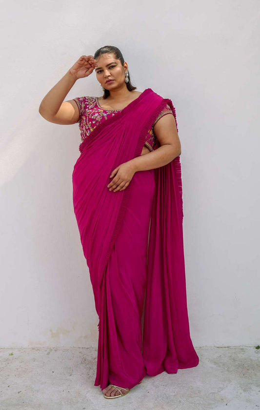 This outfit features a high-waisted skirt with attached wrap-around draping - all pre-stitched so you can put the outfit together in 30 seconds or less. The piece is paired with a pink hand-embroidered, cap-sleeve blouse with a low 